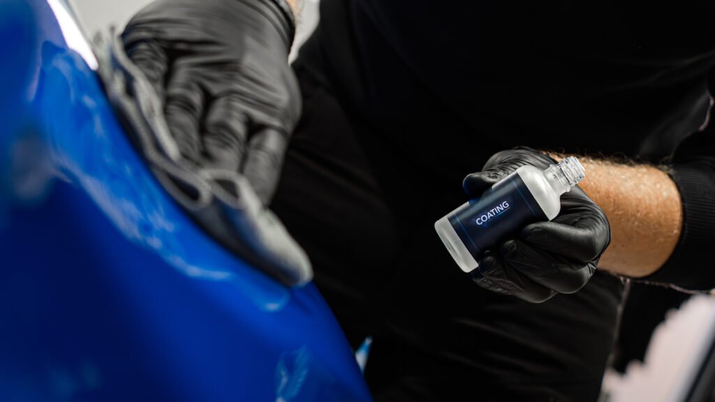 Detailer die een flesje coating vasthoud en met een microvezeldoek aanbrengt op de lak