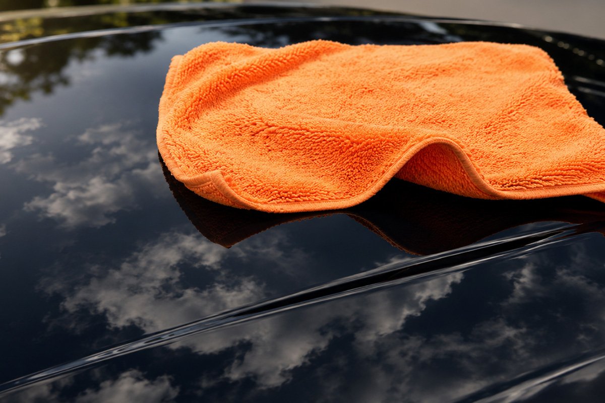 een donkere motorkap en daarop een buffingcloth die er af glijd
